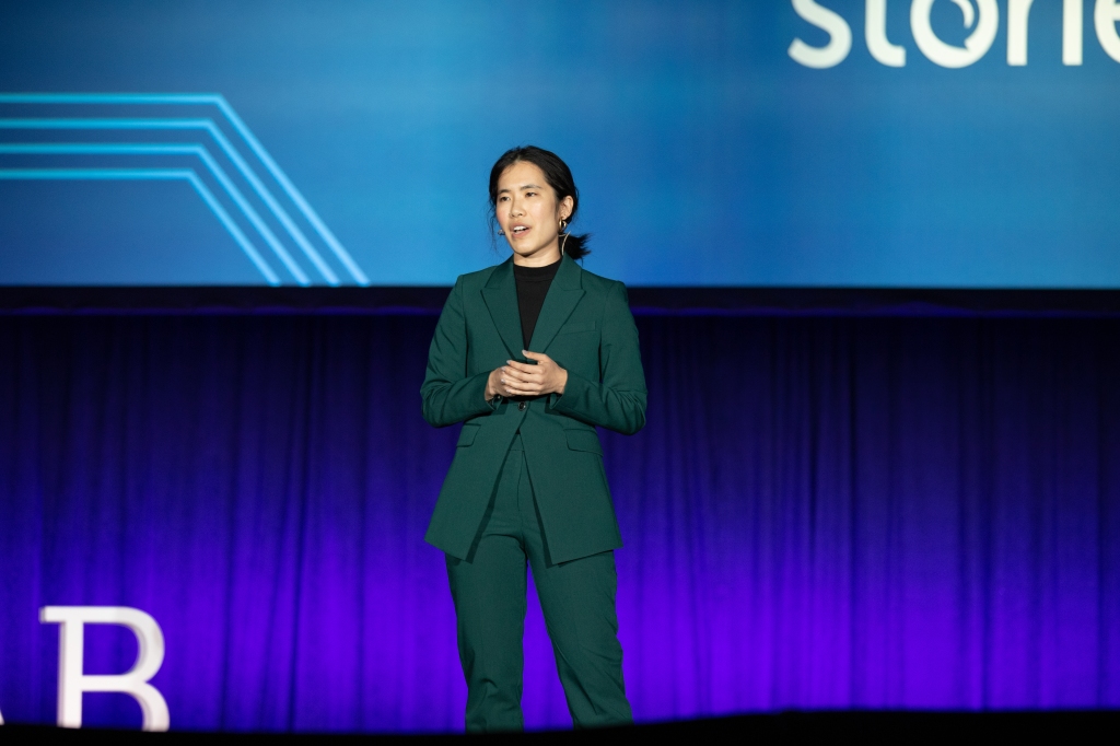 Photo of Annie in a green suit facilitating the CONNECTED stories session on stage at a conference.